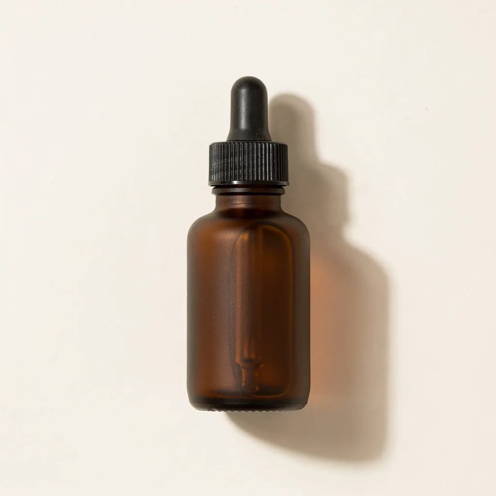 An unbranded amber glass dropper bottle with a black cap on an off-white background
